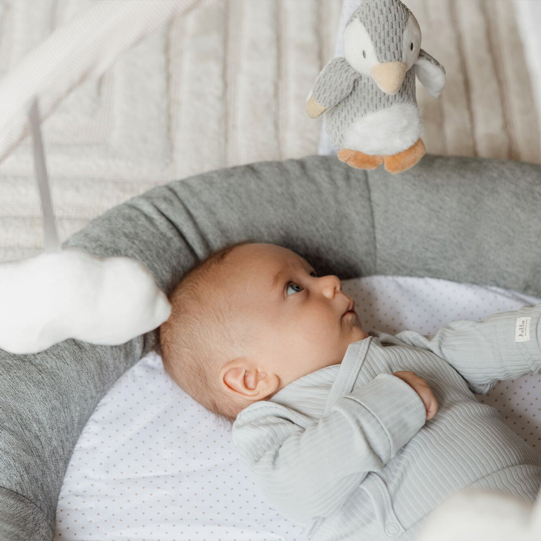 A baby looking at a plush penguin that is hanging down from part of the Penguin Pals Play Gym created by Nuby.