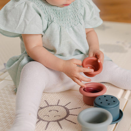 A young baby sat up on their Play Mat decorated in things from the sky including a happy sun, a product by Nuby.