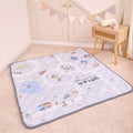 The Quilted Playmat, featuring cheerful vehicle and animal designs, rests on a beige carpet. Next to it stands a wooden side table with towels, while colorful decorative bunting hangs above.