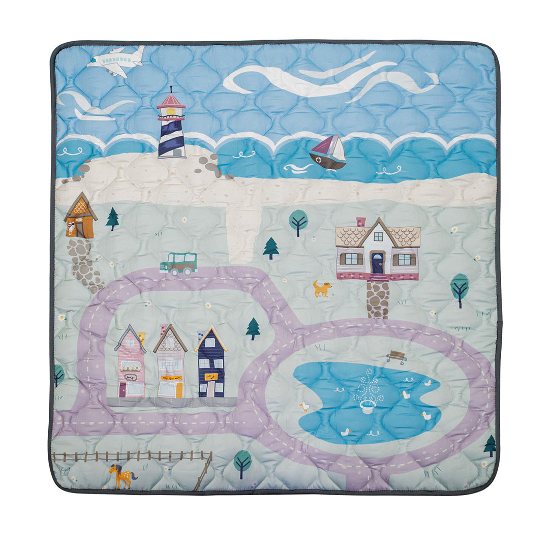 The Quilted Playmat features a vibrant scene with a lighthouse, sea, boat, houses, winding road, pond with ducks, trees, cat, dog, and birds beneath a cloudy sky—ideal as a cozy play space for babies.