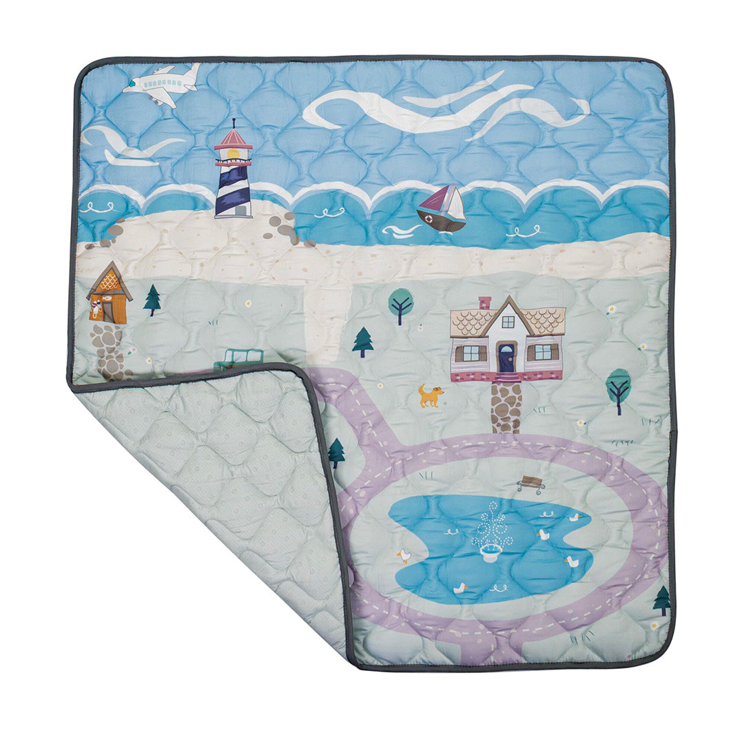 The Quilted Playmat features vibrant scenes with a lighthouse, sailboat, plane, beach, house, pond with ducks, and winding paths. Soft and padded for comfort, it’s perfect for little explorers to play and discover. One corner is shown folded over.