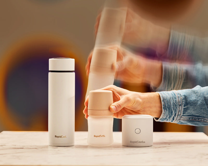 A man's hand from the Milk Race advertisement aired by Nuby. This includes a RapidBottle being placed onto a table at a child's play area inbetween both a RapidCool and a RapidSterilise+. The man is wearing a blue denim jacket.