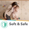 A mother and baby relax on the Nuby Foldable Play Mat, Stars, featuring soft comfort with star and rainbow designs. The mother smiles at her baby holding her hand. Text below reads “Soft & Safe” with a green shield icon.