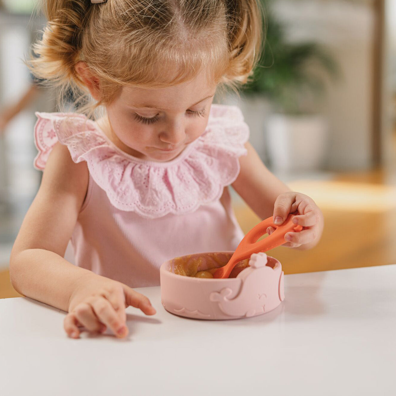 The easy grip spoons by Nuby sat on a table top as part of a young child having a meal by using them. They are scooring up fruit with their spoon.