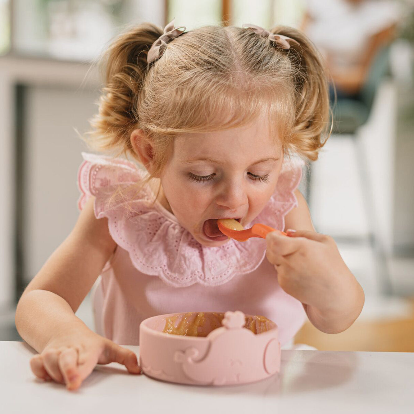 The easy grip spoons by Nuby sat on a table top as part of a young child having a meal by using them. They are bringing the spoon to their face to help them eat.