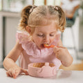The easy grip spoons by Nuby sat on a table top as part of a young child having a meal by using them. They are bringing the spoon to their face to help them eat.