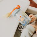 A baby using the Super Straw sippy cup from Nuby. Holding it in front of a baby seat.