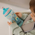 The Super Slurp bottle in a blue and pink colourway decorated in rainbow style animals with a young child looking at the bottle while they hold it.