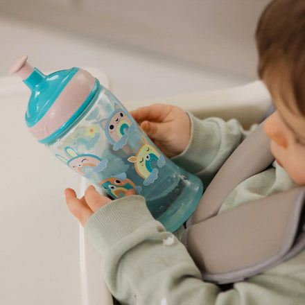 The Super Slurp bottle in a blue and pink colourway decorated in rainbow style animals with a young child looking at the bottle while they hold it.