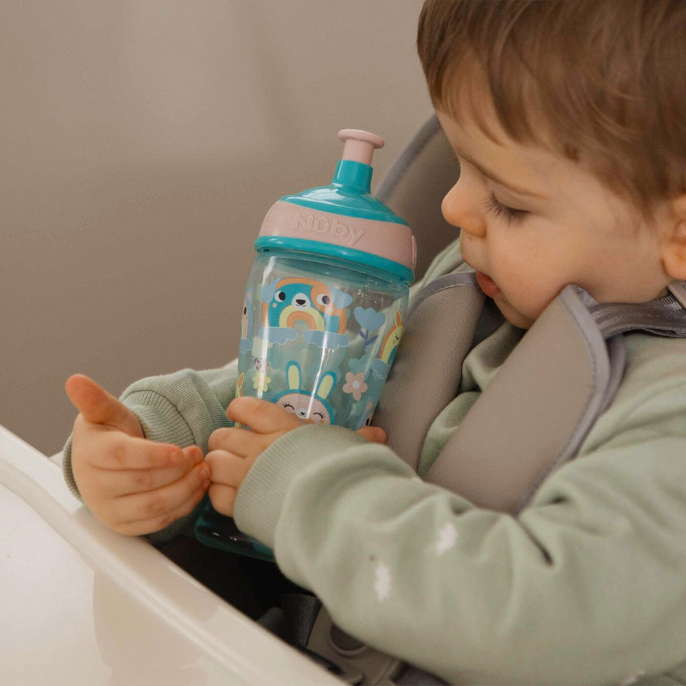 The Super Slurp bottle in a blue and pink colourway decorated in rainbow style animals with a young child looking at the bottle while they hold it close to themselves.