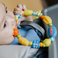 A baby in a blue outfit chews on a colorful teether from the Nuby UK Teether Bundle while sitting in a high chair.