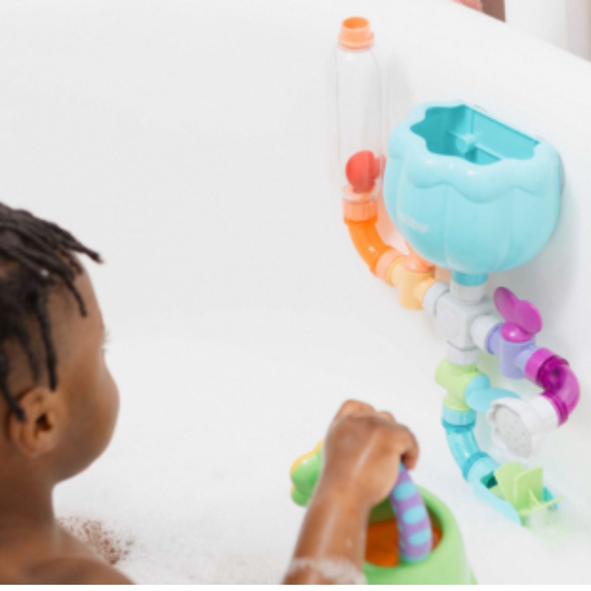 A child in a bathtub plays with the Wacky Pipes Bath Toy attached to the wall, enjoying its colorful tubes, gears, and spinning parts that let water flow through—making bath time extra fun with this engaging toy.