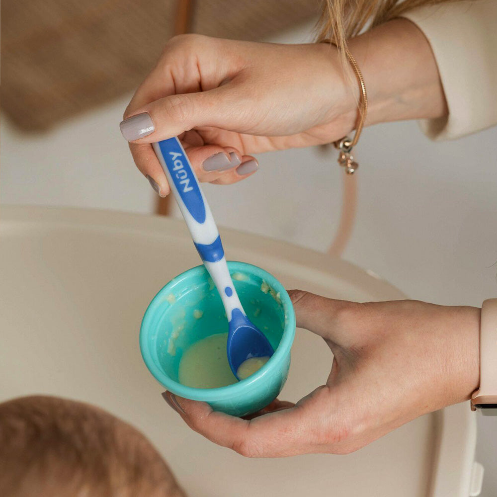 A woman's hand holding the blue Weaning Spoon by Nuby.