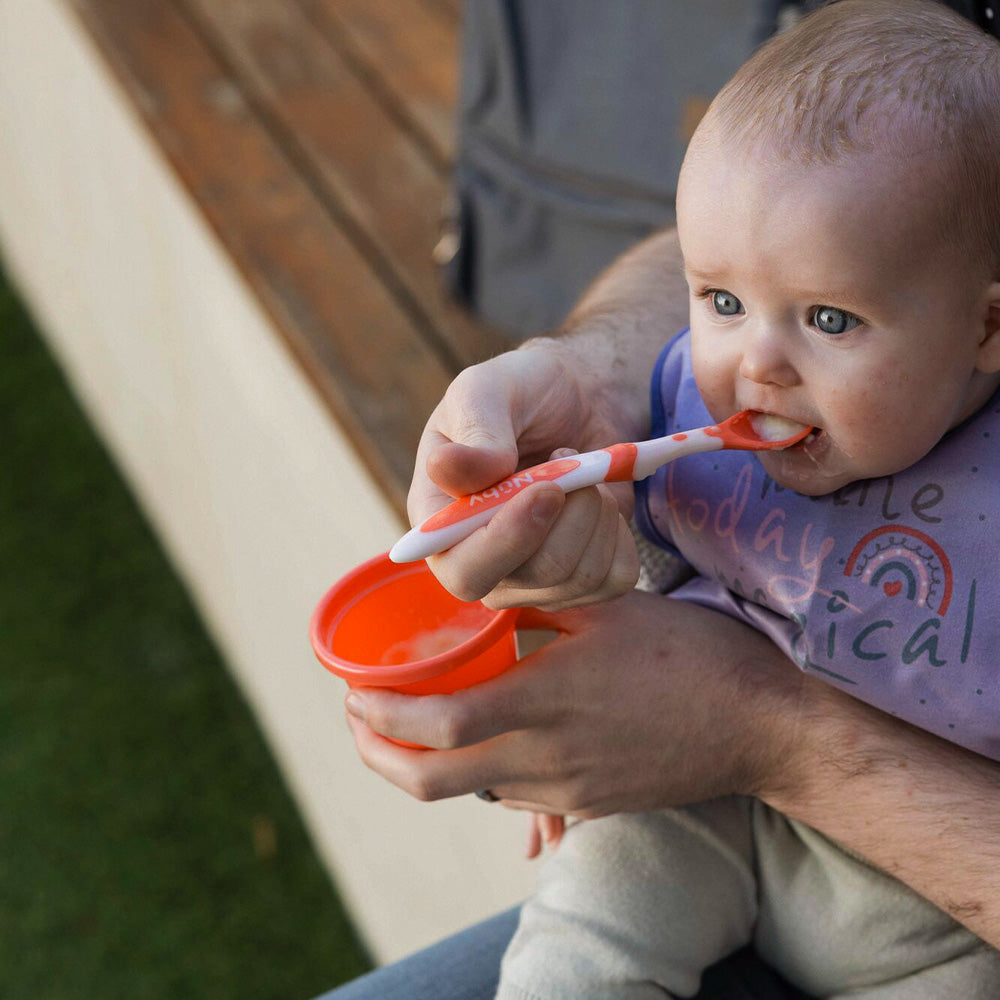A young child eating from their Weaning Spoon by Nuby in an orange colour.