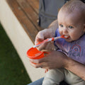 A young child eating from their Weaning Spoon by Nuby in an orange colour.