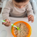A young child using their Nuby weaning spoon in a green colour to eat some oats.