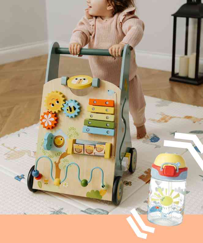 Baby using a wooden walker in a living room setting with a picture of a sippy cup in front of the baby walker.
