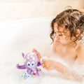 A young child with curly hair plays with a purple octopus from the Nuby UK Bath Toy Bundle 12 Months+ in a bubble-filled tub, focused on the toy and surrounded by white foam.