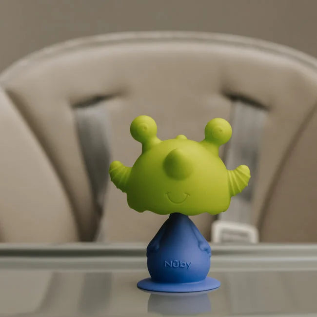 The Nuby Bobble Highchair & Teething Toy, a green and blue alien-shaped silicone teether with suction base, rests on the highchair tray, with the padded seat visible in the background.