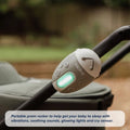 The Nuby UK Jitterbug Pram Rocker attaches to a stroller handle, features easy-to-use buttons and a glowing light, and is shown outdoors with text highlighting its soothing, calming abilities.