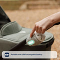 A hand holds the light gray Nuby UK Jitterbug Pram Rocker with a glowing green light above a stroller handle. Text reads: Portable with USB rechargeable battery.