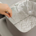 A hand places a metal rack inside a gray insulated cooler bag with reflective silver lining, ideal for storing your Nuby UK RapidCool™ Kit and UV Steriliser Bundle or other baby feeding essentials.