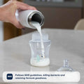 A hand pours milk from RapidCool™ Baby Bottle Maker by Nuby into a baby bottle—ideal for travel feeding. A nipple rests nearby. Text: Follows NHS guidelines, killing bacteria and retaining formula goodness. Twin Pack included.