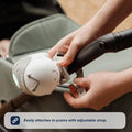 Close-up of hands attaching the Nuby UK Jitterbug Pram Rocker to a pram handle using its adjustable strap. Text below reads: Easily attaches to prams with adjustable strap.