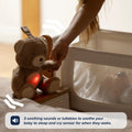 A person places the Nuby UK Biscuit Bear Baby Sleep Aid with Cry Sensor near a sleeping baby. Text: “3 soothing sounds or lullabies and gentle white noise help soothe your baby to sleep, plus a cry sensor for wake-ups.”.