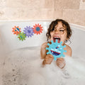 A young child laughs in a bubble bath, holding a blue ship-shaped foam piece from the Nuby UK Bath Toy Bundle 12 Months +. Colorful puzzle pieces from the set stick to the tiled wall above the tub.