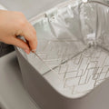 A hand lifts a metal rack from a gray, insulated container with a shiny silver interior, resembling the design of the Nuby 3 Minute UV Baby Steriliser.